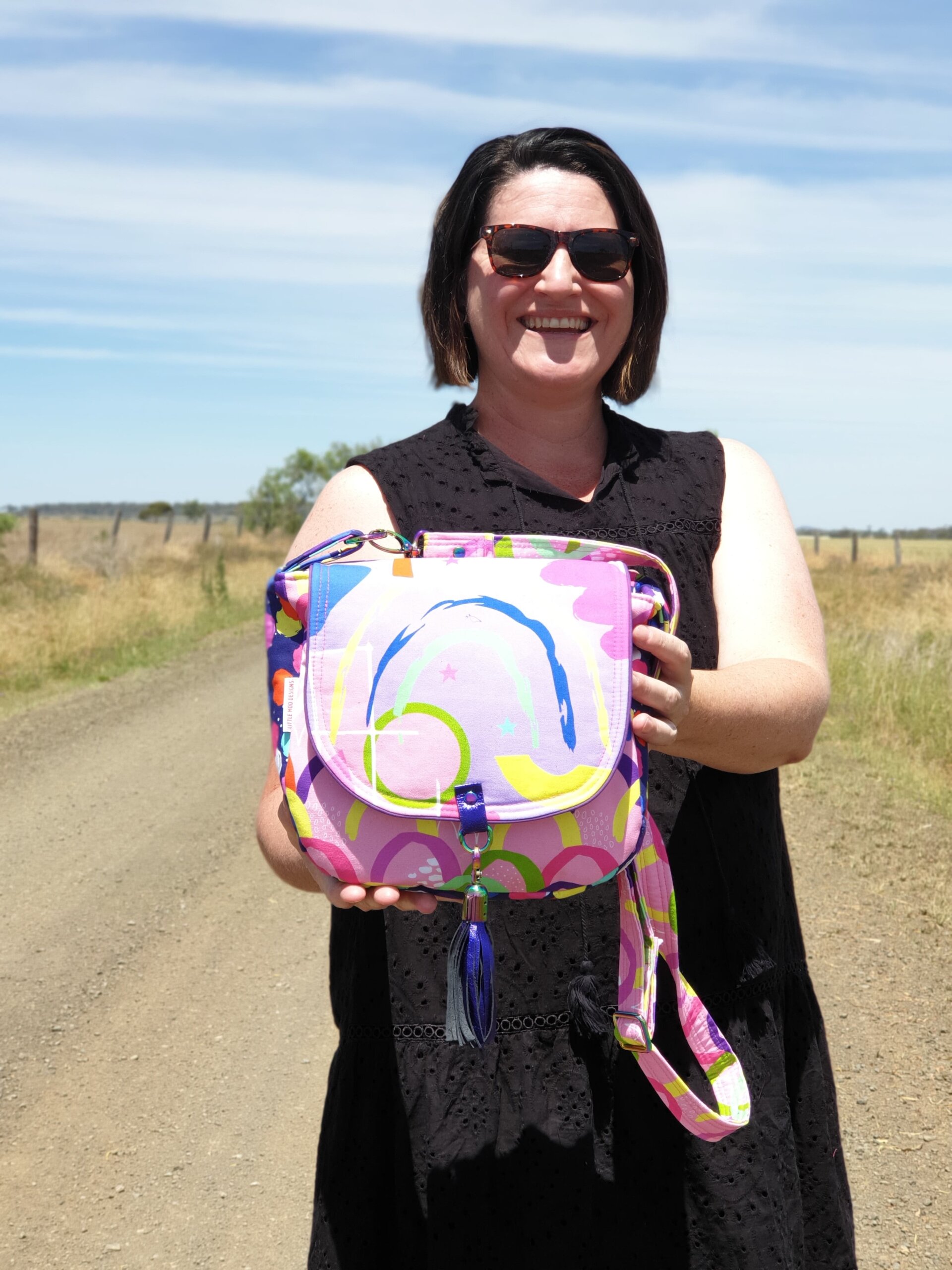 Kylie, the owner of Little Moo Designs standing on the road in front of her farm, holding a Matilda Saddle Bag. 